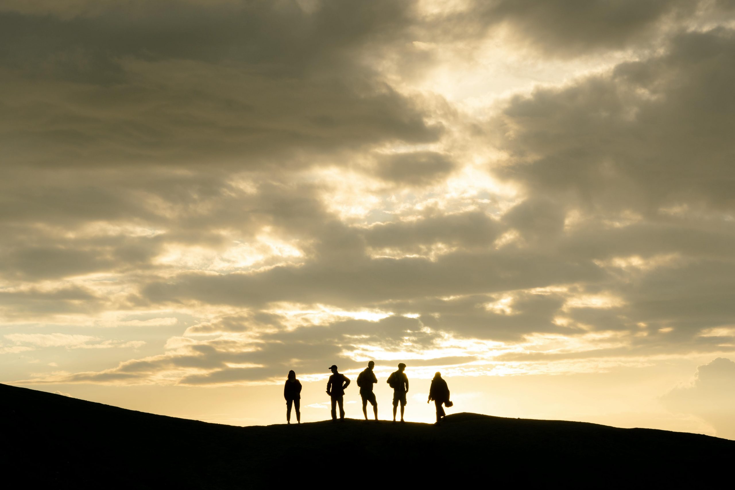 Group of hikers silhouetted on a mountain under a dramatic cloudy sunset sky.