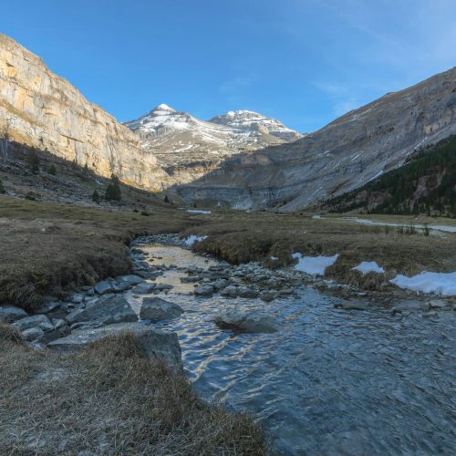Breathtaking landscape of Ordesa Valley with snow-capped mountains and clear stream in Spanish Pyrenees.